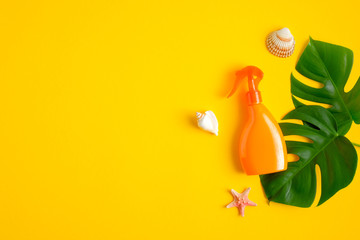 Sunscreen spray lotion orange bottle, green tropical leaves, seashells on yellow background. Sun protection and skin care concept. Flat lay, top view