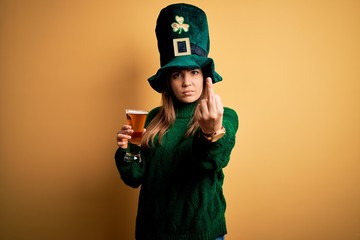 Young beautiful woman wearing green hat drinking glass of beer on saint patricks day Showing middle...