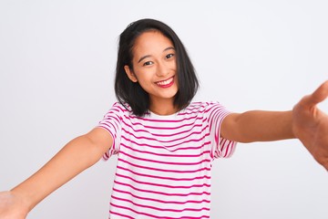 Young chinese woman wearing striped t-shirt standing over isolated white background looking at the camera smiling with open arms for hug. Cheerful expression embracing happiness.