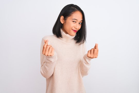 Young chinese woman wearing turtleneck sweater standing over isolated white background doing money gesture with hands, asking for salary payment, millionaire business