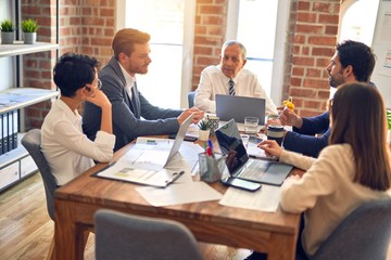 Group of business workers working together. Sitting on desk using laptop and talking at the office