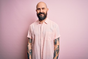 Handsome bald man with beard and tattoo wearing casual shirt over isolated pink background Relaxed with serious expression on face. Simple and natural looking at the camera.