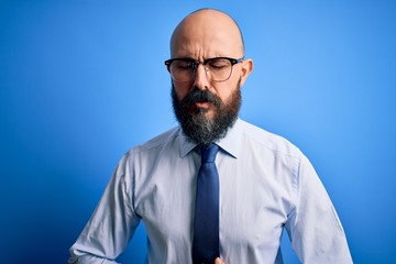 Handsome business bald man with beard wearing elegant tie and glasses over blue background with hand on stomach because indigestion, painful illness feeling unwell. Ache concept.