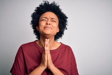 Young beautiful African American afro woman with curly hair wearing casual t-shirt standing begging...