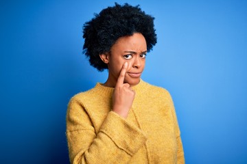 Fototapeta na wymiar Young beautiful African American afro woman with curly hair wearing yellow casual sweater Pointing to the eye watching you gesture, suspicious expression