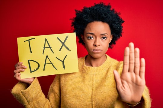 Young African American afro woman with curly hair holding paper with tax day message with open hand doing stop sign with serious and confident expression, defense gesture