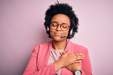 Young African American call center operator woman with curly hair using headset smiling with hands...