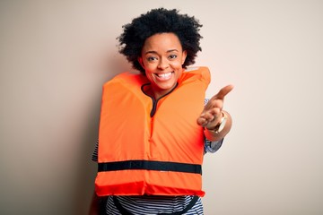 Young African American afro woman with curly hair wearing orange protection lifejacket smiling friendly offering handshake as greeting and welcoming. Successful business.