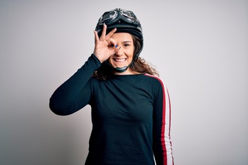 Beautiful motorcyclist woman with curly hair wearing moto helmet over white background doing ok gesture with hand smiling, eye looking through fingers with happy face.