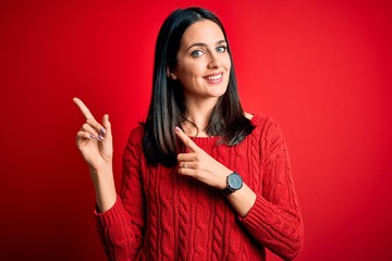 Young brunette woman with blue eyes wearing casual sweater over isolated red background smiling and looking at the camera pointing with two hands and fingers to the side.