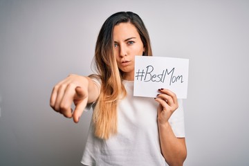 Young beautiful woman holding paper with best mom message celebrating mothers day pointing with...