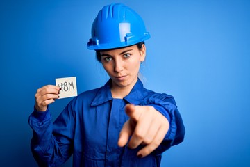 Beautiful worker woman wearing hardhat and uniform celebrating 8th march womens day pointing with finger to the camera and to you, hand sign, positive and confident gesture from the front