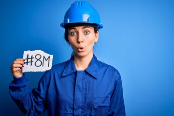 Beautiful worker woman wearing hardhat and uniform celebrating 8th march womens day scared in shock...