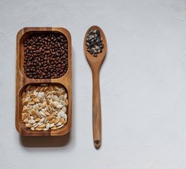 Pine nuts and pumpkin seeds in a wooden bowl and a large wooden spoon with sunflower seeds on a white background, on top