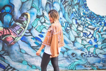 Young beautiful girl wearing brown jacket standing backwards over colorful wall  at the town street