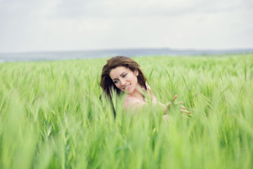 Young pretty woman in dress poses on summer wheat field. Smiling girl on green meadow. Freedom