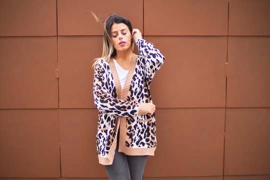 Young beautiful girl wearing animal print cardigan leaning on the wall at the town street, standing with relaxed face