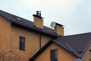 part of a brown brick private house with windows under a tiled roof and two chimneys against the sky