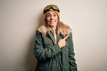 Young brunette skier woman wearing snow clothes and ski goggles over white background Pointing...