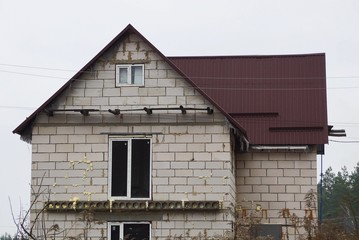 the attic of a private house of white bricks with windows on the wall under a brown tiled roof against the sky