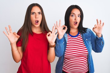 Young beautiful women wearing casual clothes standing over isolated white background looking surprised and shocked doing ok approval symbol with fingers. Crazy expression