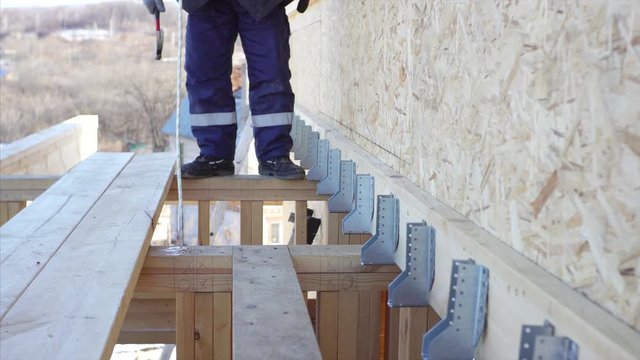 Row of metal angles. Builder is fixing metal angles on wooden bulks with nails and manual hummer. Frame house under construction