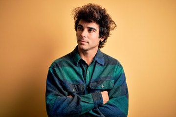 Young handsome man wearing casual shirt standing over isolated yellow background looking to the side with arms crossed convinced and confident