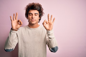 Young handsome man wearing casual t-shirt standing over isolated pink background relaxed and smiling with eyes closed doing meditation gesture with fingers. Yoga concept.