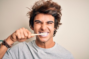 Young handsome man smiling happy. Standing with smile on face whasing tooth using toothbrush over...