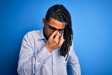 Young handsome african american man with dreadlocks wearing casual shirt and glasses tired rubbing nose and eyes feeling fatigue and headache. Stress and frustration concept.