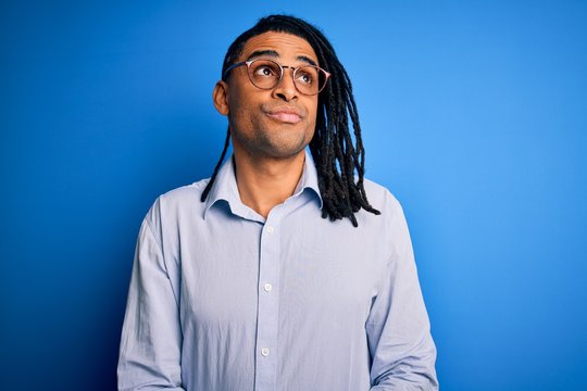 Young handsome african american man with dreadlocks wearing casual shirt and glasses smiling looking to the side and staring away thinking.