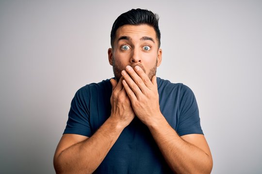 Young handsome man wearing casual t-shirt standing over isolated white background shocked covering mouth with hands for mistake. Secret concept.