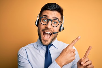 Young business operator man wearing customer service headset from call center smiling and looking at the camera pointing with two hands and fingers to the side.