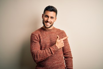 Young handsome man wearing casual sweater standing over isolated white background cheerful with a smile on face pointing with hand and finger up to the side with happy and natural expression