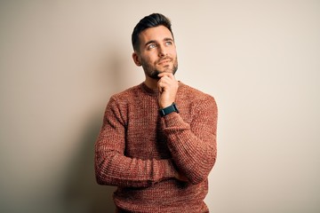 Young handsome man wearing casual sweater standing over isolated white background with hand on chin thinking about question, pensive expression. Smiling and thoughtful face. Doubt concept.