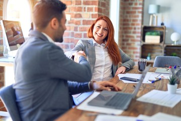 Young beautiful couple of business workers smiling happy and confident. Shaking hands with smile on face for agreement at office