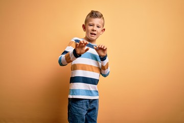 Young little caucasian kid with blue eyes wearing colorful striped shirt over yellow background...
