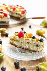 Moostorte aus grünem Biscuit mit Quark, Sahne, Früchte, Blaubeere, Himbeere, Physalis auf Holz