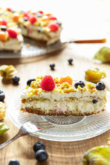 Moostorte aus grünem Biscuit mit Quark, Sahne, Früchte, Blaubeere, Himbeere, Physalis auf Holz