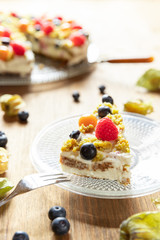 Moostorte aus grünem Biscuit mit Quark, Sahne, Früchte, Blaubeere, Himbeere, Physalis auf Holz