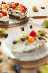 Moostorte aus grünem Biscuit mit Quark, Sahne, Früchte, Blaubeere, Himbeere, Physalis auf Holz