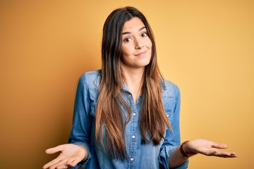 Young beautiful girl wearing casual denim shirt standing over isolated yellow background clueless...