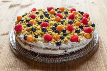 Moostorte aus grünem Biscuit mit Quark, Sahne, Früchte, Blaubeere, Himbeere, Physalis auf Holz