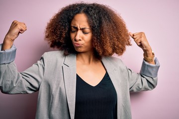 Young african american businesswoman with afro hair wearing elegant jacket showing arms muscles smiling proud. Fitness concept.