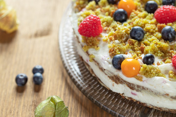 Moostorte aus grünem Biscuit mit Quark, Sahne, Früchte, Blaubeere, Himbeere, Physalis auf Holz