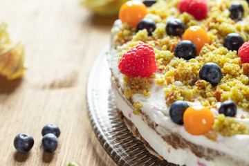 Moostorte aus grünem Biscuit mit Quark, Sahne, Früchte, Blaubeere, Himbeere, Physalis auf Holz