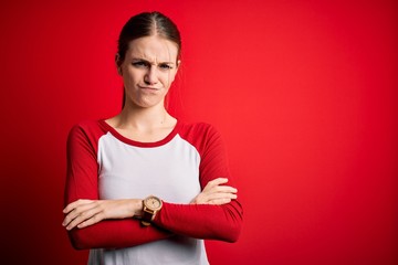 Young beautiful redhead woman wearing casual t-shirt over isolated red background skeptic and...