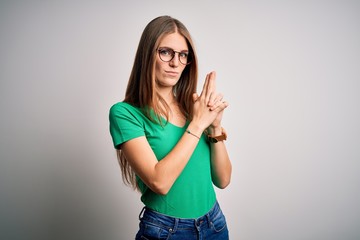 Young beautiful redhead woman wearing casual green t-shirt and glasses over white background Holding symbolic gun with hand gesture, playing killing shooting weapons, angry face