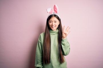 Young asian woman wearing cute easter bunny ears over pink background showing and pointing up with fingers number four while smiling confident and happy.