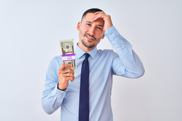 Young handsome business man holding a bunch of dollars bank notes over isolated background stressed with hand on head, shocked with shame and surprise face, angry and frustrated. Fear and upset